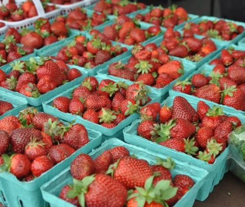 Fresh strawberries in green containers arranged on a table at a market.