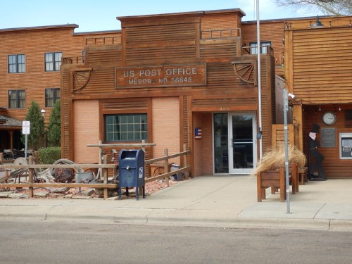Exterior of a wooden US Post Office building in Medora, ND, featuring a blue mailbox and rustic design elements.