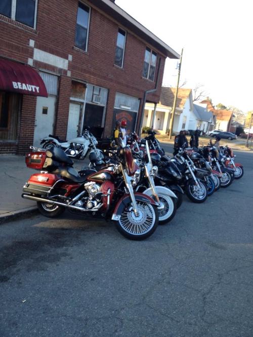 A row of parked motorcycles lined up along a street in front of a brick building with a "Beauty" sign.