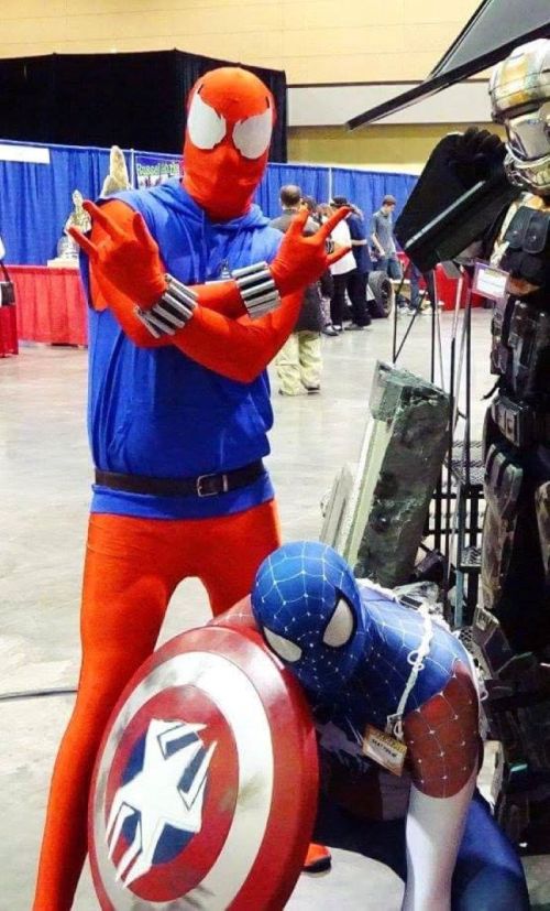 Two costumed characters at a convention: one in a red and blue Spider-Man suit, the other in a blue suit with a shield.