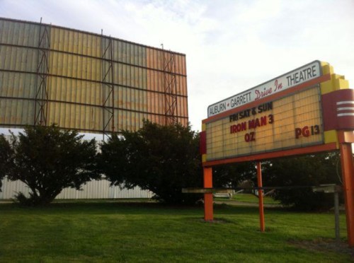A vintage drive-in theater marquee displays "Iron Man 3" and "Oz" with a large screen in the background.