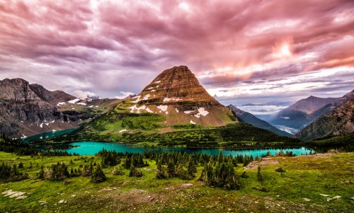 A stunning mountain landscape at sunset, featuring a vibrant lake and dramatic clouds in the sky.