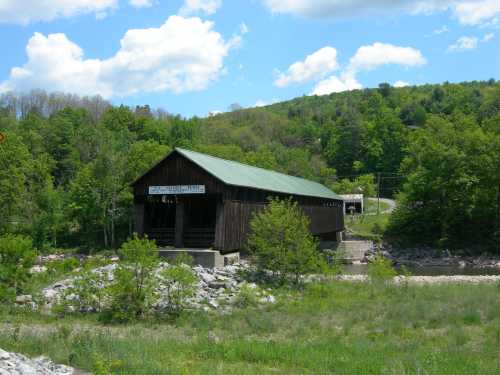 A wooden covered bridge surrounded by lush green trees and a clear blue sky with fluffy clouds.