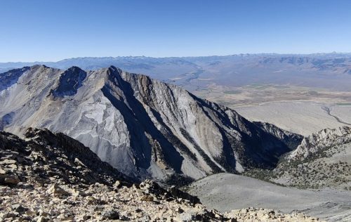 A panoramic view of rugged mountains and valleys under a clear blue sky.