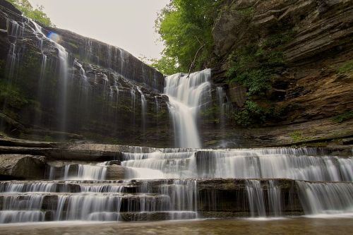 A serene waterfall cascading over rocky ledges, surrounded by lush greenery and a misty atmosphere.