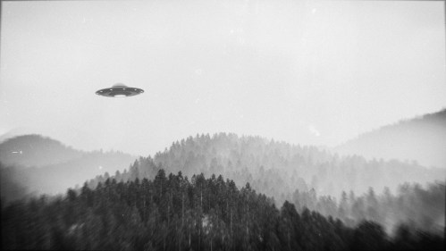 A black and white image of a UFO hovering over misty mountains and dense forests.