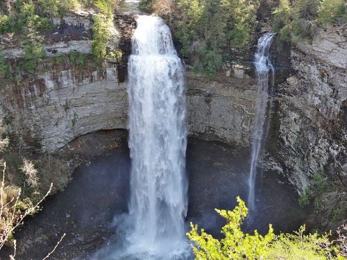 A scenic view of a waterfall cascading into a rocky basin, surrounded by lush greenery and cliffs.