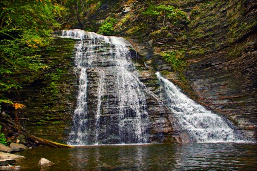 A serene waterfall cascading down rocky cliffs into a calm pool, surrounded by lush greenery.