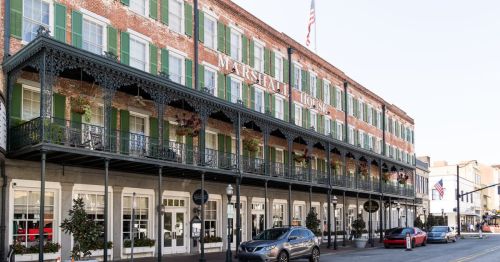 Historic brick building with green shutters and a decorative balcony, featuring the sign "Marshall House" and parked cars.