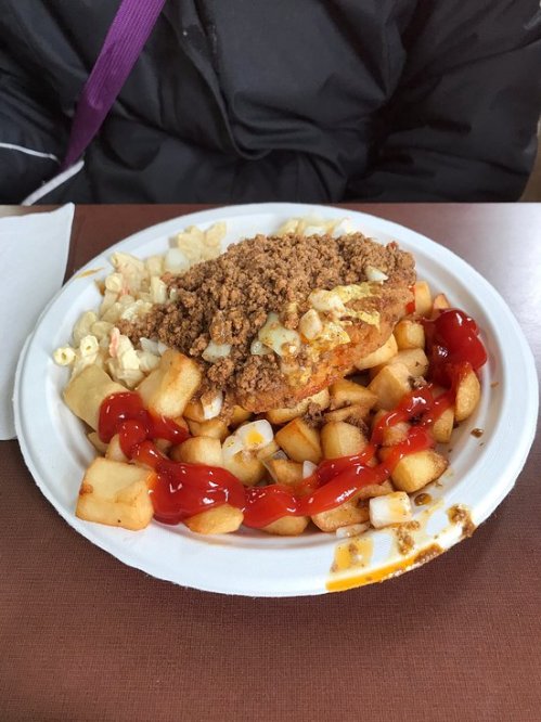 A plate of fried chicken topped with crumbled toppings, served with diced potatoes and ketchup.