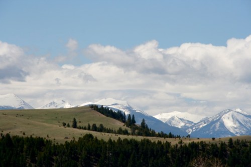 Snow-capped mountains rise above green hills under a partly cloudy sky.