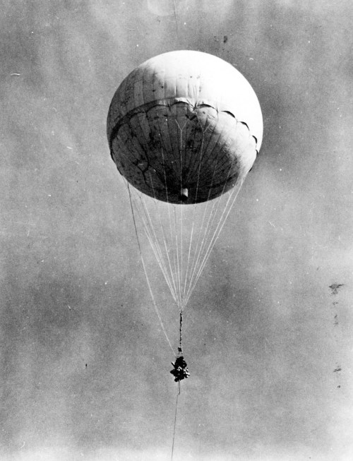 A vintage black and white photo of a hot air balloon ascending against a cloudy sky.