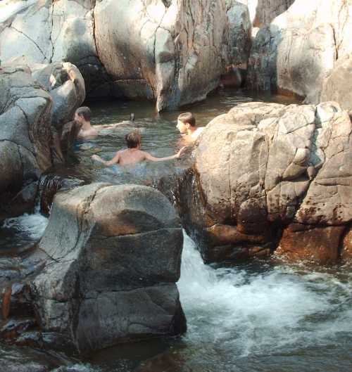 Four people enjoying a natural pool surrounded by large rocks and flowing water.