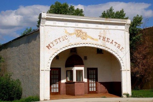 Exterior of the Mystic Theatre, featuring an arched entrance and faded signage against a blue sky.