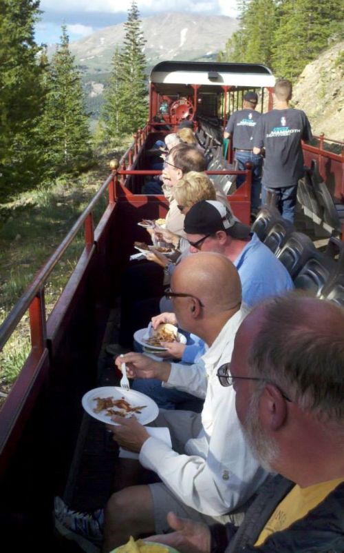A group of people enjoying a meal on a train ride through a scenic, mountainous landscape.