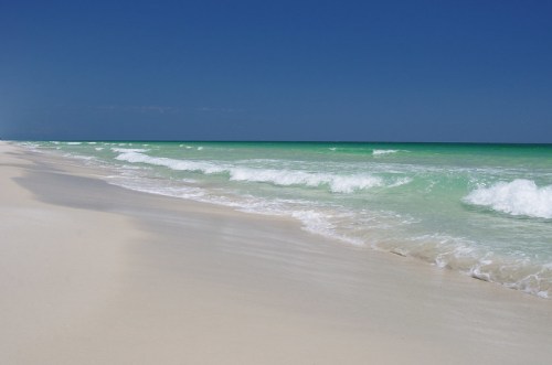 A serene beach with soft white sand and gentle turquoise waves under a clear blue sky.