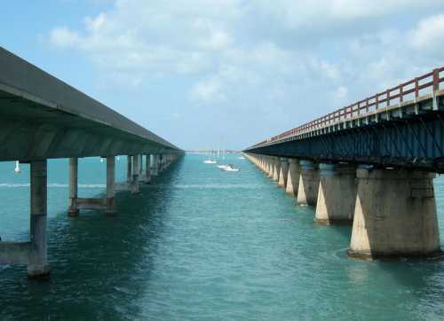 Two parallel bridges over turquoise water, supported by concrete pillars, under a blue sky with scattered clouds.