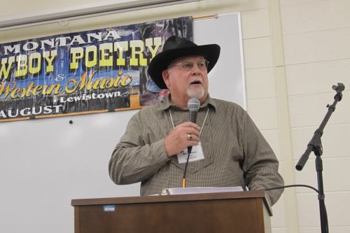 A man in a black hat speaks at a podium during a cowboy poetry and music event in Montana.