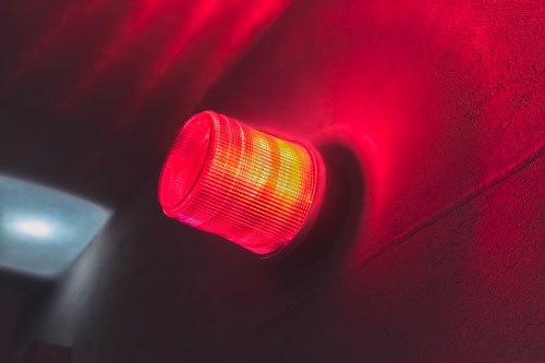 A red emergency light mounted on a wall, glowing brightly in a dimly lit corridor.
