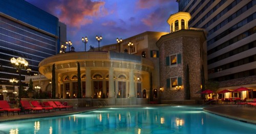 A luxurious hotel pool area at dusk, featuring elegant architecture and red lounge chairs by the water.