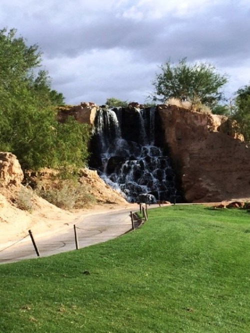 A serene waterfall cascading over rocky terrain, surrounded by greenery and a winding path.