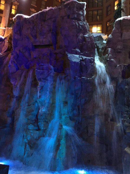 A cascading waterfall over rocky terrain, illuminated with blue and purple lights, creating a serene atmosphere.