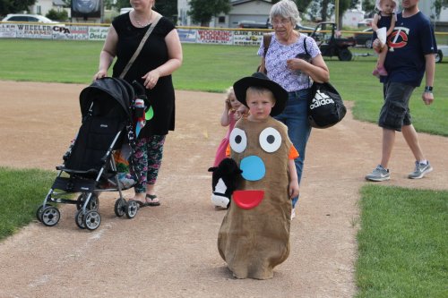 A child in a potato costume walks on a baseball field, accompanied by adults and other children.