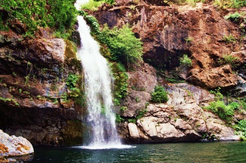 A serene waterfall cascading down rocky cliffs, surrounded by lush greenery and reflecting in a calm pool below.