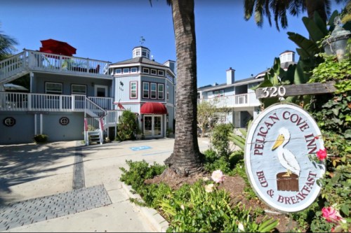 A charming bed and breakfast with a sign, palm trees, and colorful flowers in a sunny outdoor setting.