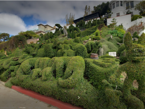 A lush hillside garden featuring intricately shaped topiary plants in various forms and sizes.