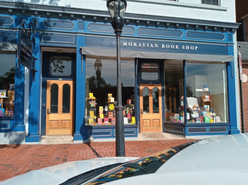 Exterior of Moravian Book Shop with large windows displaying books, colorful signs, and a lamp post in front.