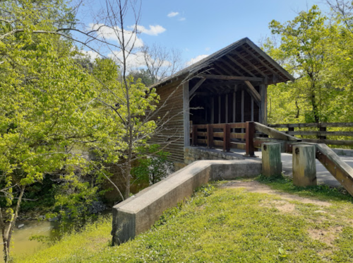 A wooden covered bridge surrounded by lush greenery and a clear blue sky.