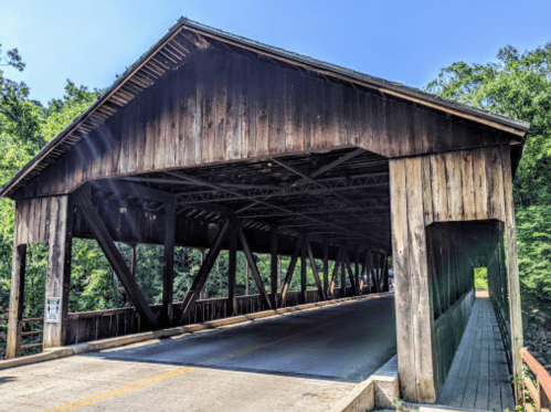A wooden covered bridge with a clear sky and trees in the background, showcasing its rustic architecture.