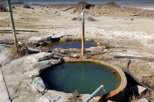 Two circular, stone-lined pools filled with water, surrounded by dry, barren land and sparse vegetation.