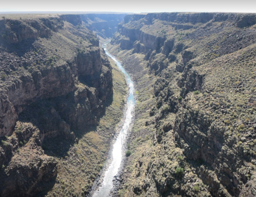 A winding river flows through a deep canyon surrounded by rugged cliffs and sparse vegetation under a clear sky.