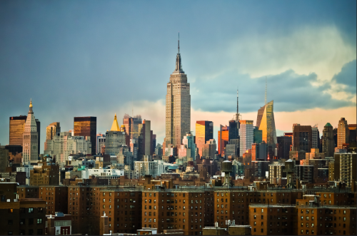 A panoramic view of the New York City skyline featuring the Empire State Building and various skyscrapers at sunset.