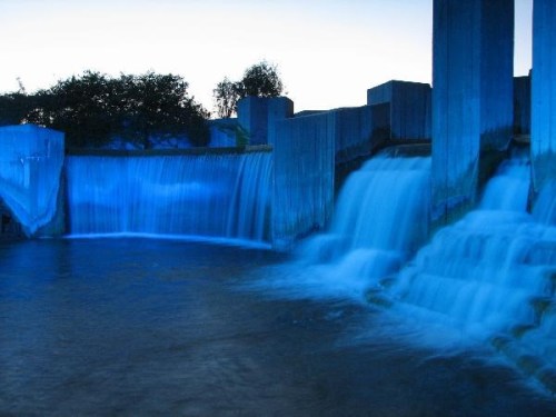 A serene waterfall illuminated in blue, cascading over concrete structures into a calm body of water.