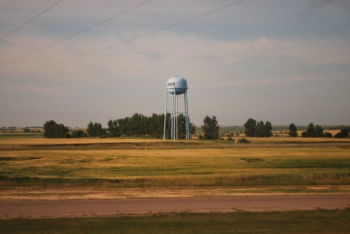 A blue water tower stands in a grassy field, surrounded by trees under a cloudy sky.