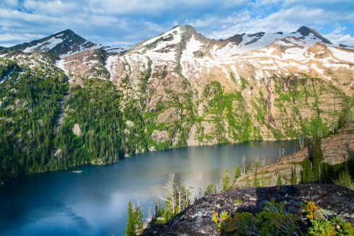 A serene mountain landscape featuring a clear lake surrounded by snow-capped peaks and lush greenery.