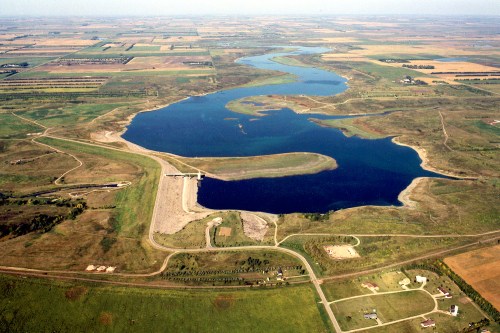 Aerial view of a winding river surrounded by green fields and farmland, with a dam and roads visible.
