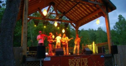 A band performs on stage at Rooster Walk, surrounded by trees and illuminated by hanging lights.