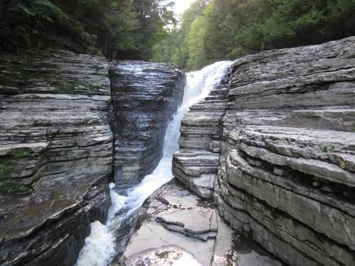 A cascading waterfall flows over layered rock formations surrounded by lush greenery.