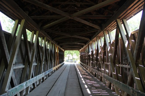 Interior view of a wooden covered bridge, showcasing beams and sunlight filtering through the structure.