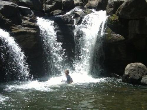A person splashes in a natural pool beneath a waterfall, surrounded by rocks and flowing water.