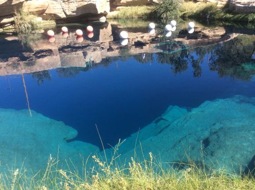 A clear blue pond surrounded by rocky cliffs, with red and white buoys floating on the water's surface.