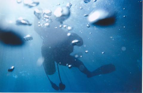 A diver swimming underwater, surrounded by bubbles and blue water, creating a serene aquatic scene.