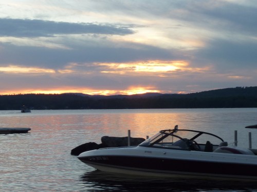 A serene sunset over a lake, with a boat in the foreground and silhouettes of hills in the background.