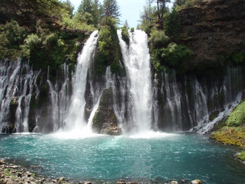 A scenic waterfall cascading into a turquoise pool, surrounded by lush greenery and rocky cliffs.