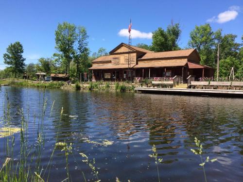 A rustic wooden building by a calm pond, surrounded by trees and blue skies, with an American flag flying.