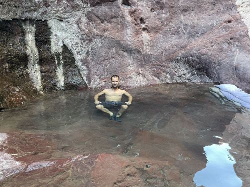 A person sitting in a natural pool surrounded by rocky terrain, enjoying the serene water.